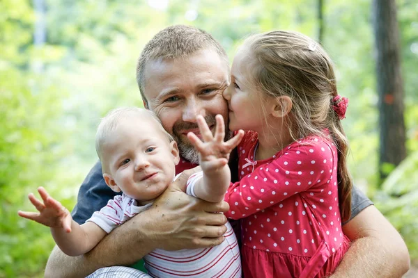 Hingebungsvoller Vater umarmt seinen Sohn und seine Tochter und genießt das Outdoor. — Stockfoto