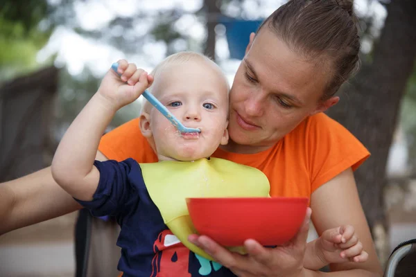 Jongen in moeders schoot op de camping, eten in Camping klapstoel, plezier in de buitenlucht. — Stockfoto