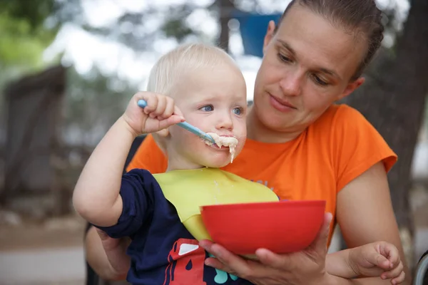 Jongen in moeders schoot op de camping, eten in Camping klapstoel, plezier in de buitenlucht. — Stockfoto