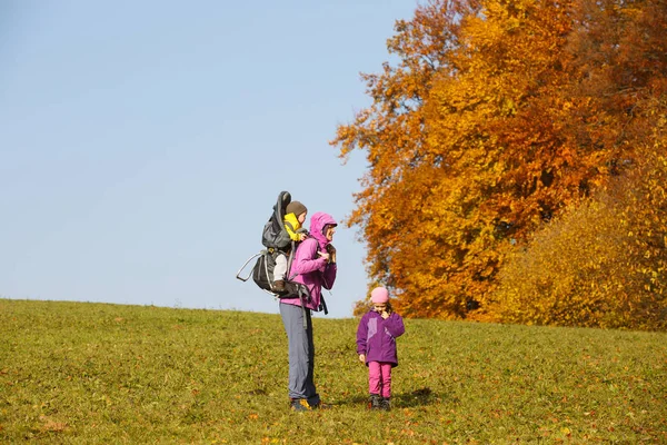 Madre con niños senderismo en un bonito día de otoño llevando niño — Foto de Stock