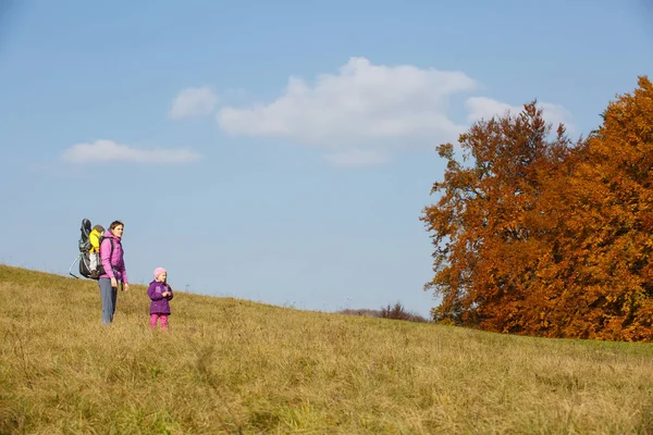 Mother with children hiking on a nice autumn day carrying kid — Stock Photo, Image