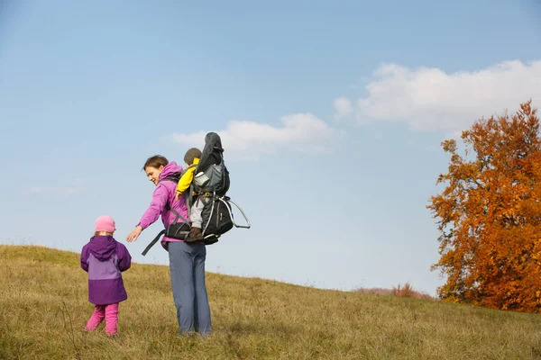 Мама з дітьми ходить в гарний осінній день, що несе дитину — стокове фото