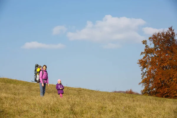 Mother with children hiking on a nice autumn day carrying kid — Stock Photo, Image