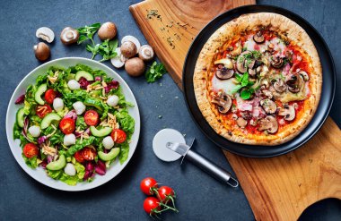 Pizza ve salat tahtadan yapılma tahtadan yapılma taş bir zeminde yemeye hazır.