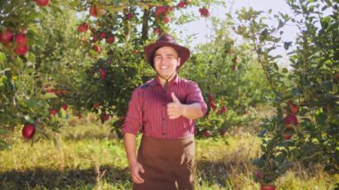 Elma bahçesinde yukarı başparmak gösterilen çiftçi dans. Gülümseyen ve dans Genç çiftçi