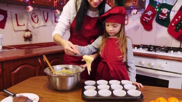 Mother help her daughter puts a raw dough into white paper form for cupcake. — Stock Video