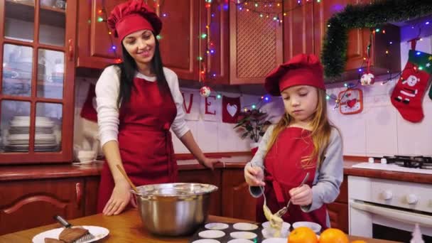 Mother help her daughter puts a raw dough into white paper form for cupcake. — Stock Video