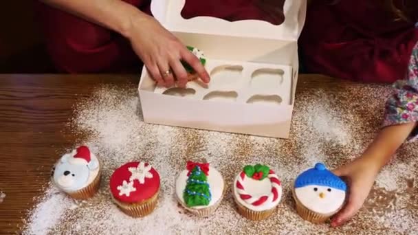 Hands of mother and her daughter put amazing Christmas cupcakes into the box. — Stock Video