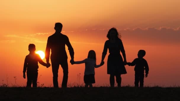 Siluetas de familia feliz caminando juntos en el prado durante el atardecer — Vídeo de stock