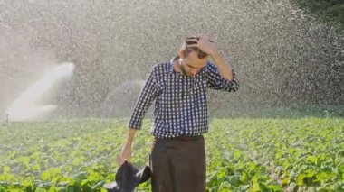 Yorgun çiftçi şapkasını alır ve eller plantasyon sulama sırasında yükseltir