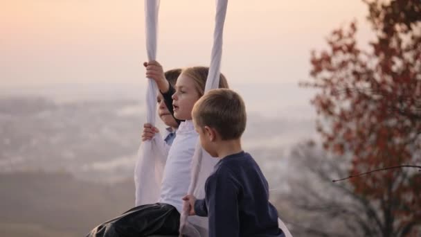 Två pojkar skakar sin lillasyster på en gunga under ett stort träd. — Stockvideo