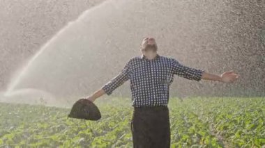 Çiftliğinde mi çiftçi ve ellerini yukarı yükseltir. Mutlu çiftçi başarı iş sulama sistemi sırasında zevk. Su fıskiyesi, bir çiftçi alır