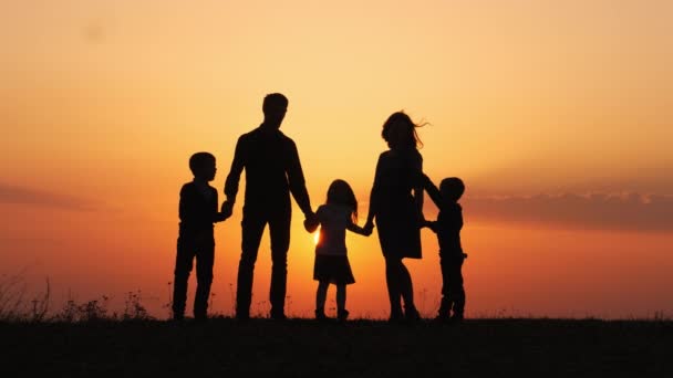 Silhuetas de família feliz segurando as mãos no prado durante o pôr do sol . — Vídeo de Stock