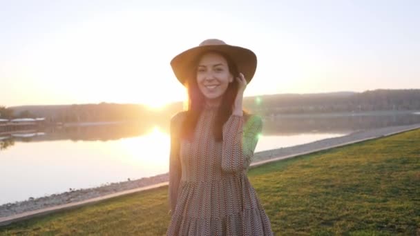 Adorabile ragazza con cappello sorridente posa davanti alla macchina fotografica vicino al lago — Video Stock