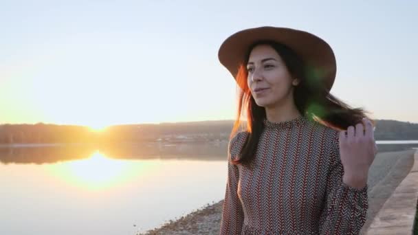 Adorable joven con sombrero sonriendo posando en la cámara cerca del lago — Vídeos de Stock