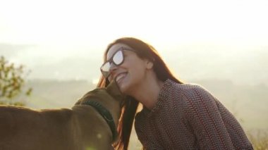 Güzel kız yavaşça onun sevimli köpek okşayarak güneş gözlüğü. Çok güzel genç kadın ile köpek niteliğine şaşırtıcı günbatımı sırasında oynamaya. Ağır çekim.