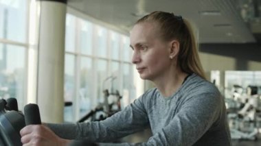 Orta yaş spor salonunda egzersiz bisikleti üzerinde çekici kadın.
