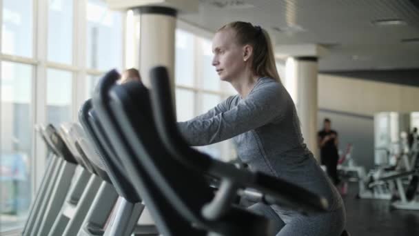 Orta yaş spor salonunda egzersiz bisikleti üzerinde çekici kadın. — Stok video