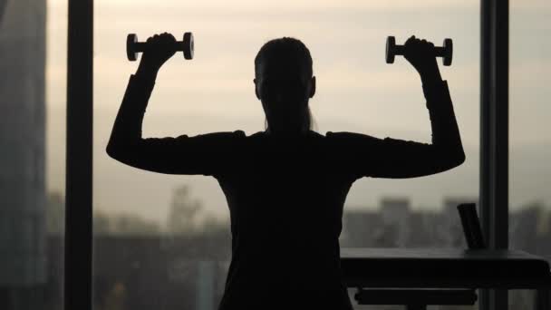 Силуэт женщины среднего возраста, делающей упражнения с гантелями . — стоковое видео