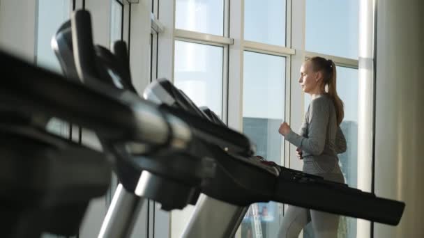 Atractiva mujer de mediana edad se ejecuta en el molino de rodadura en el gimnasio deportivo — Vídeos de Stock