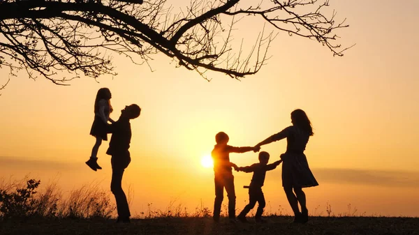 Siluetas de familia pasando tiempo juntos en el prado cerca durante el atardecer —  Fotos de Stock