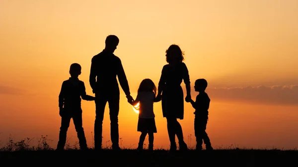 Silhouetten einer glücklichen Familie, die sich bei Sonnenuntergang auf der Wiese an den Händen hält. — Stockfoto