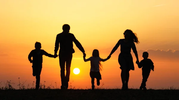 Siluetas de familia feliz sosteniendo las manos en el prado durante el atardecer . —  Fotos de Stock