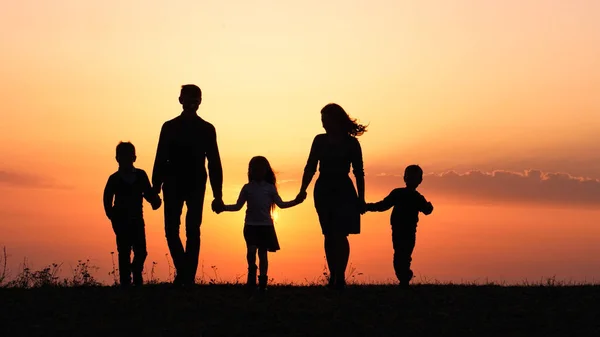 Siluetas de familia feliz sosteniendo las manos en el prado durante el atardecer . —  Fotos de Stock