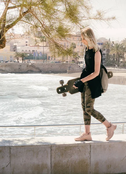 Bella ragazza con uno skateboard nelle mani a piedi lungo il lungomare. — Foto Stock