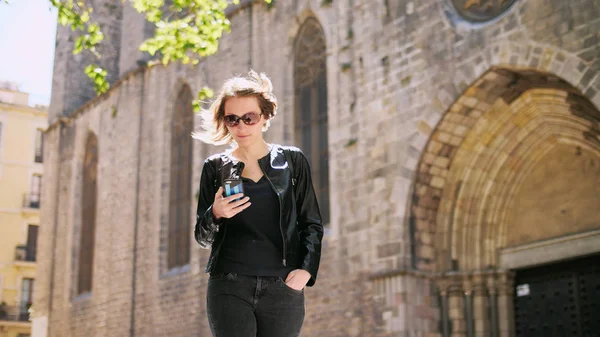 Felice ragazza utilizza uno smartfone mentre cammina per strada nella giornata di sole. — Foto Stock