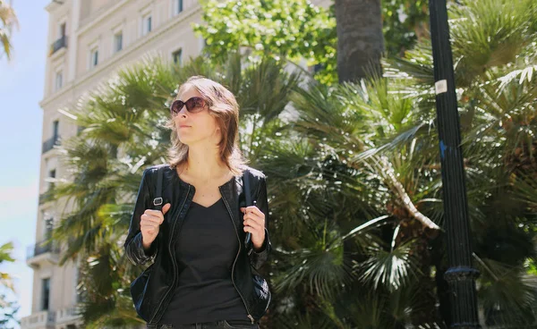 Attraente donna turistica in occhiali da sole con zaino passeggiando per strada . — Foto Stock