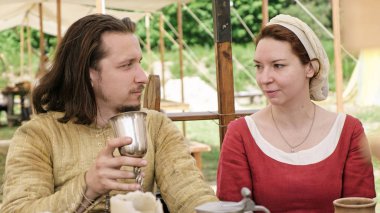 Ortaçağ kıyafetleri giymiş bir grup insan masada otururken birlikte vakit geçiriyorlar..