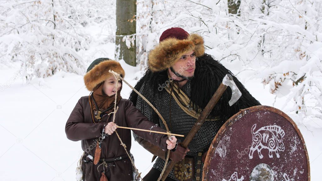Father viking teach his son to archery in the winter forest.