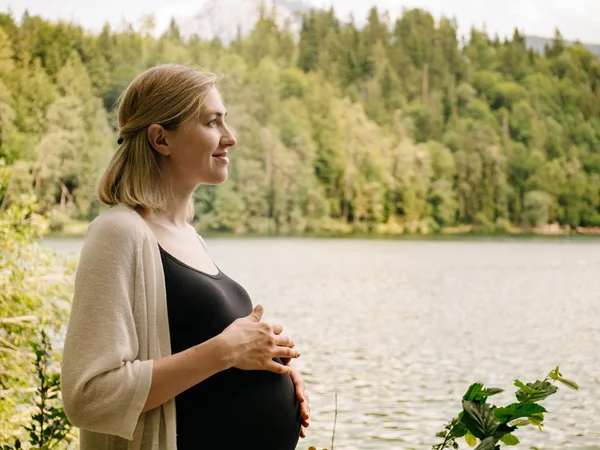 Vacker gravid kvinna nära en fjällsjö i skogen. — Stockfoto