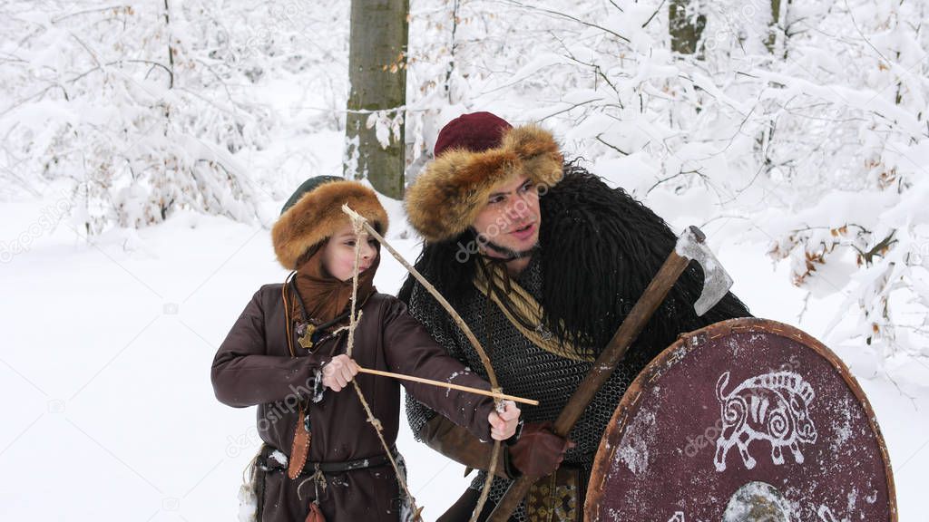 Father viking teach his son to archery in the winter forest.