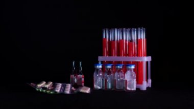 Kırmızı sıvı ve siyah arkaplan ampullü test tüpleri üzerine haplar.