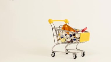 Beyaz arka planda tıbbi kapsüllerle dolu bir süpermarket arabası.