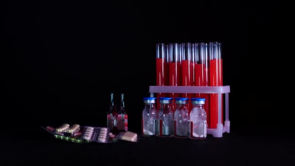 Pilules sur fond de éprouvettes avec liquide rouge et ampoules sur fond noir — Video