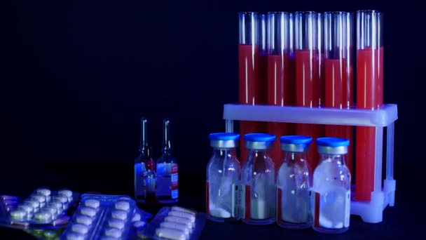 Pastillas sobre fondo de tubos de ensayo con líquido rojo y ampollas sobre fondo negro — Vídeo de stock