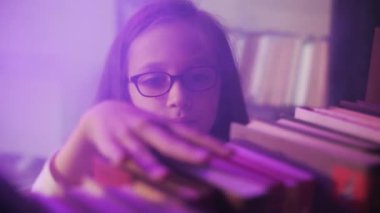 Yakın plan. Bir kız kütüphanenin raflarındaki kitapları düzenliyor..