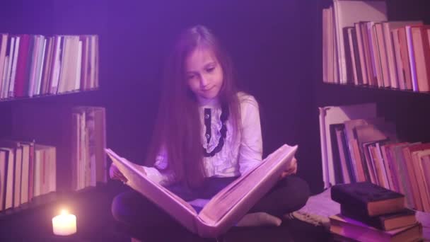 Дівчина відкриває казкову книгу в бібліотеці, кольорові димові круги навколо, свічки освітлені поруч — стокове відео