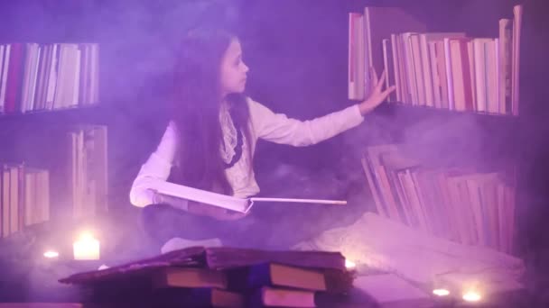 Een meisje sorteert boeken op de planken van de bibliotheek, magische rook draait rond. — Stockvideo