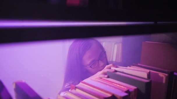 Dívka se probírá knihami na policích knihovny, magický kouř se točí kolem.