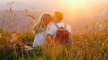 Bir dağ çayırında oturan ve gün batımının tadını çıkaran sevimli çift.