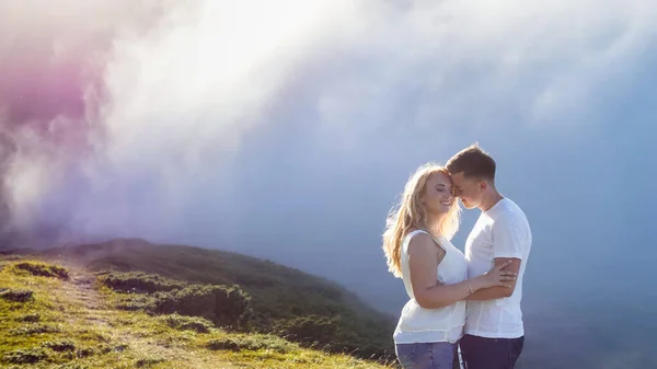 Genç çift, sisli ve güneşli arka planda, dağlık bir çayırda birbirine aşık.. — Stok fotoğraf