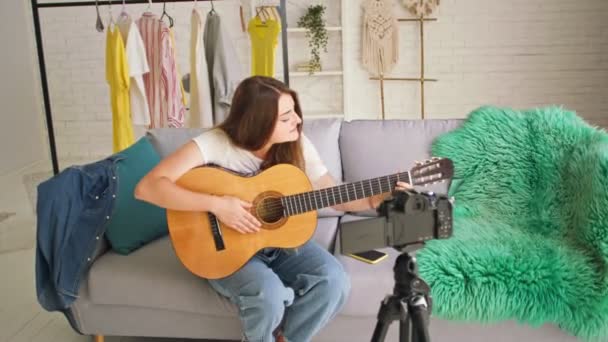 Una chica adolescente atractiva Vlogging durante el juego en una guitarra.Joven hablando mientras dispara su videoblog. Joven Conducta Enseñanza Remota para Tocar en una Guitarra Durante el Blogging. — Vídeo de stock