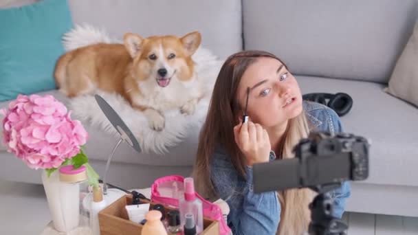 迷人的少女与她的可爱的小狗在化妆的同时，在网上发表了一篇长篇大论。年轻姑娘拍摄她美丽的录像。在写博客的过程中，年轻女孩对化妆进行远程教学. — 图库视频影像