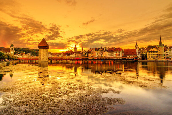 Lucerne sunset cityscape reflected in Lucerne Reuss river, Switzerland. Historic covered wooden footbridge, Chapel Bridge with Water Tower: the most famous tourist landmark.