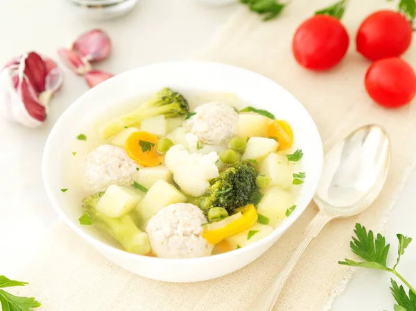 bowl of soup, a cup of broth and vegetables, meatballs made of turkey and a chicken, side view