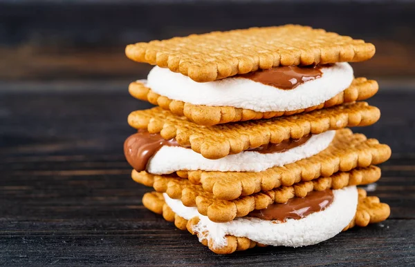 Smores, marshmallow sandwiches - traditional American sweet chocolate cookies on dark wooden table, side view